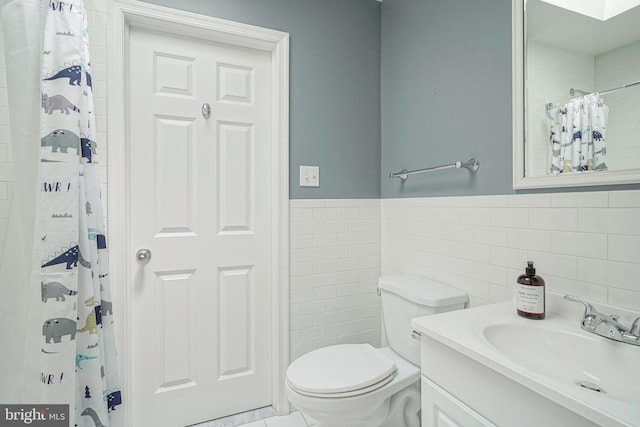 bathroom with a shower with shower curtain, vanity, toilet, and tile walls