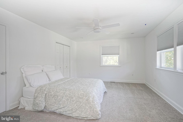 bedroom with multiple windows, ceiling fan, a closet, and light carpet