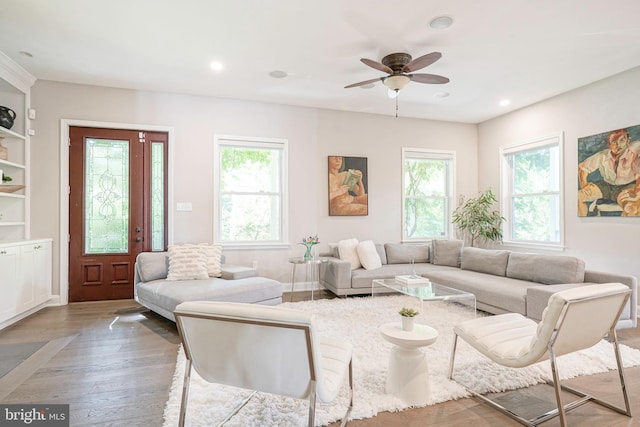 living room with hardwood / wood-style flooring, built in features, ceiling fan, and a healthy amount of sunlight