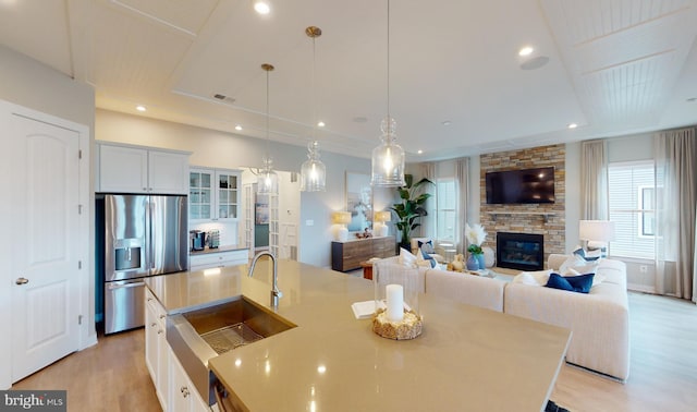 kitchen featuring white cabinetry, sink, hanging light fixtures, stainless steel fridge, and a kitchen island with sink