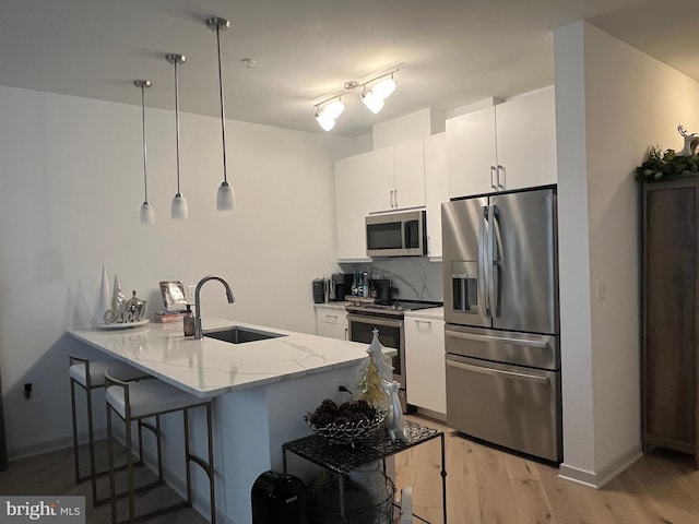 kitchen featuring kitchen peninsula, stainless steel appliances, sink, white cabinetry, and hanging light fixtures