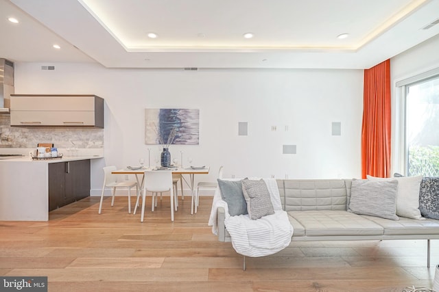 living room with light wood-type flooring and a tray ceiling