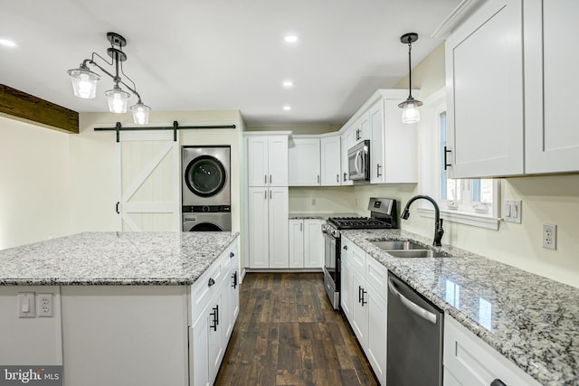 kitchen featuring pendant lighting, a barn door, stacked washer / drying machine, white cabinetry, and stainless steel appliances