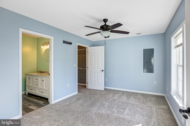 unfurnished bedroom with dark colored carpet, electric panel, ensuite bathroom, a walk in closet, and a closet