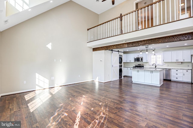 unfurnished living room featuring a towering ceiling, stacked washing maching and dryer, dark hardwood / wood-style flooring, sink, and a barn door