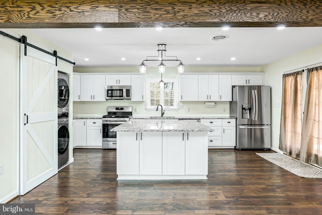 kitchen with white cabinetry, stacked washing maching and dryer, a barn door, decorative light fixtures, and appliances with stainless steel finishes