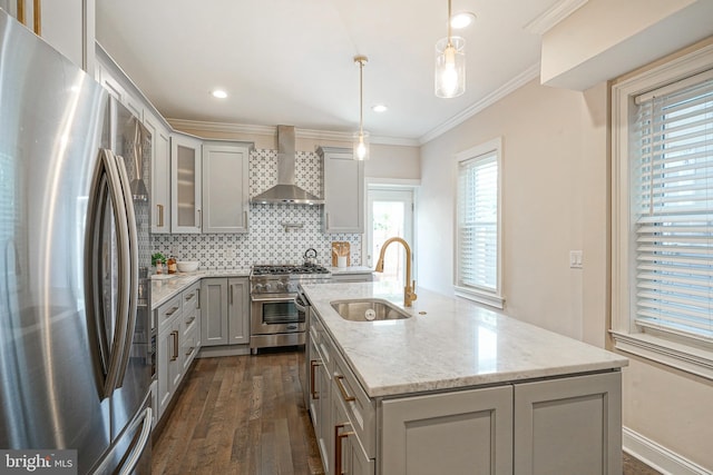 kitchen with appliances with stainless steel finishes, pendant lighting, sink, a kitchen island with sink, and wall chimney range hood