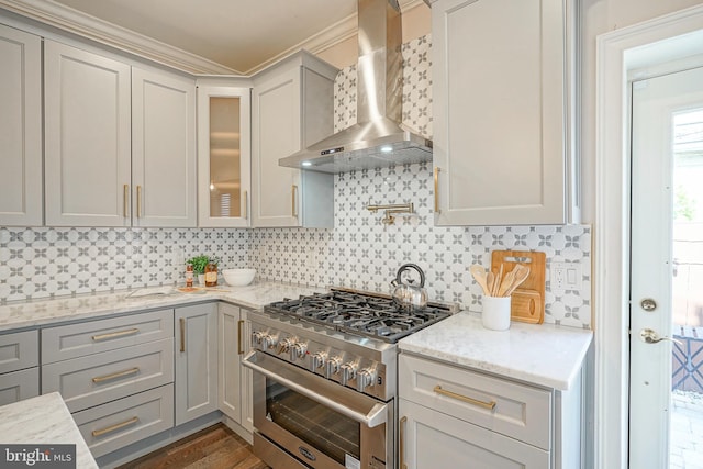 kitchen featuring tasteful backsplash, wall chimney range hood, light stone counters, and high end stove