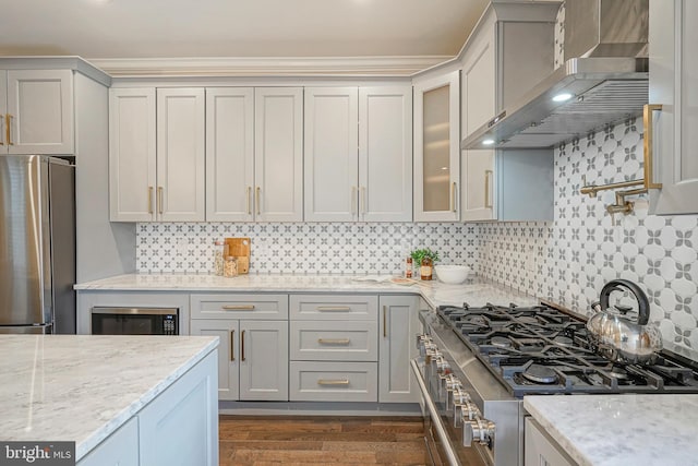 kitchen with appliances with stainless steel finishes, light stone countertops, decorative backsplash, and wall chimney range hood