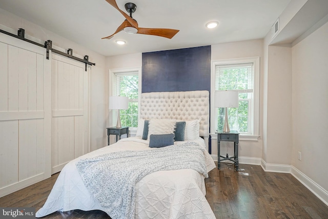 bedroom featuring dark hardwood / wood-style flooring, a barn door, and ceiling fan