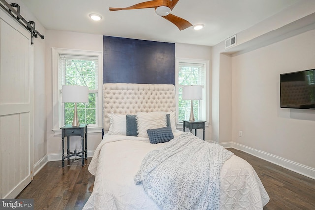 bedroom featuring ceiling fan, a barn door, dark hardwood / wood-style flooring, and multiple windows