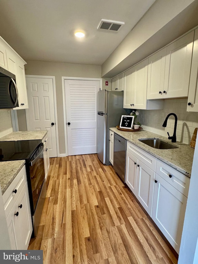 kitchen with sink, backsplash, light hardwood / wood-style floors, white cabinets, and appliances with stainless steel finishes