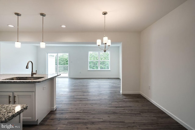 kitchen with stone countertops, sink, hanging light fixtures, and dark wood-type flooring