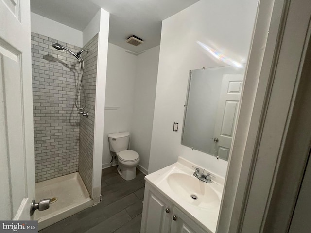 bathroom featuring vanity, hardwood / wood-style floors, toilet, and tiled shower