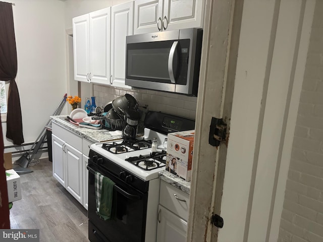 kitchen with white cabinetry, range with gas stovetop, decorative backsplash, and light wood-type flooring