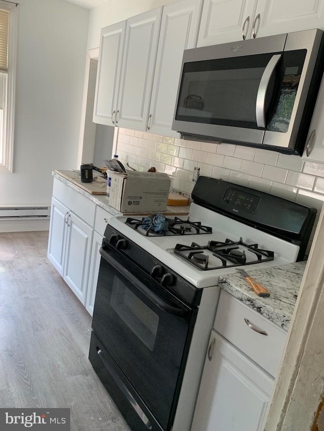 kitchen with light wood-type flooring, white cabinets, gas range oven, and decorative backsplash