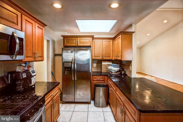 kitchen featuring a skylight, tasteful backsplash, appliances with stainless steel finishes, and brown cabinets