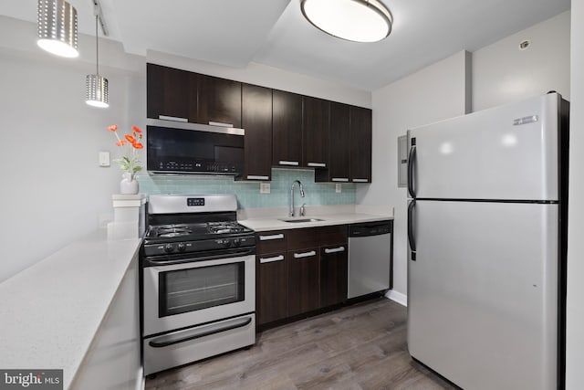 kitchen with sink, backsplash, decorative light fixtures, appliances with stainless steel finishes, and hardwood / wood-style flooring