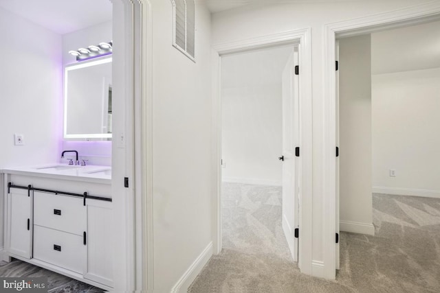 hall with light colored carpet and sink