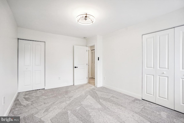 unfurnished bedroom featuring multiple closets and light colored carpet