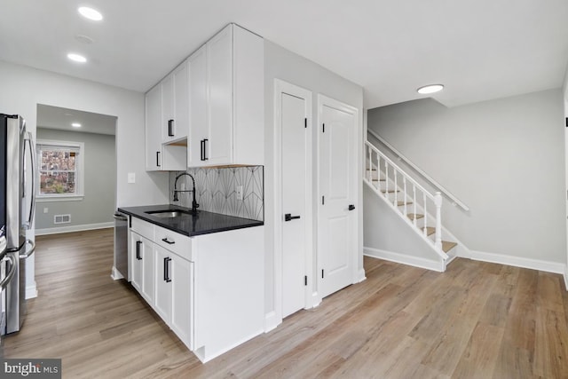 kitchen featuring appliances with stainless steel finishes, tasteful backsplash, sink, white cabinets, and light hardwood / wood-style floors