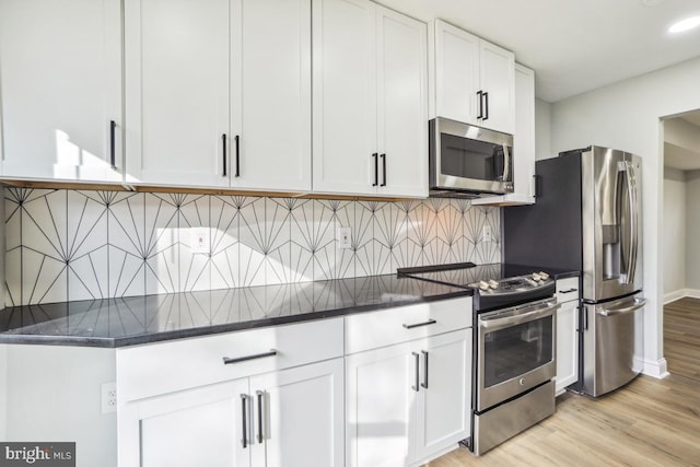 kitchen with decorative backsplash, appliances with stainless steel finishes, light wood-type flooring, dark stone counters, and white cabinetry