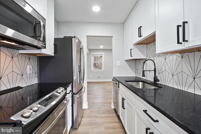 kitchen with white cabinetry, sink, dark stone countertops, appliances with stainless steel finishes, and light wood-type flooring