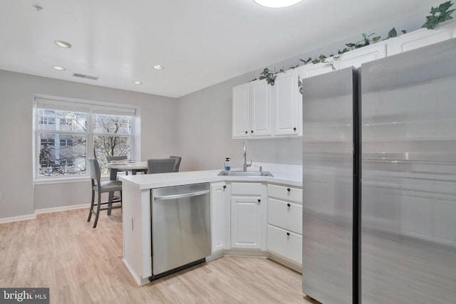 kitchen featuring kitchen peninsula, appliances with stainless steel finishes, sink, light hardwood / wood-style flooring, and white cabinetry