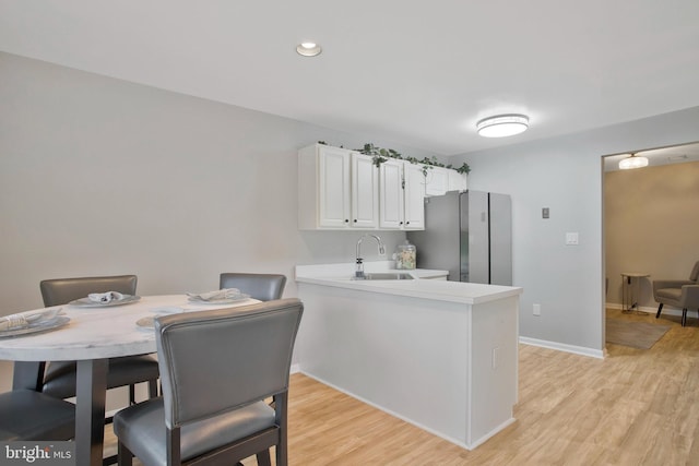 kitchen with stainless steel refrigerator, sink, light hardwood / wood-style flooring, kitchen peninsula, and white cabinets