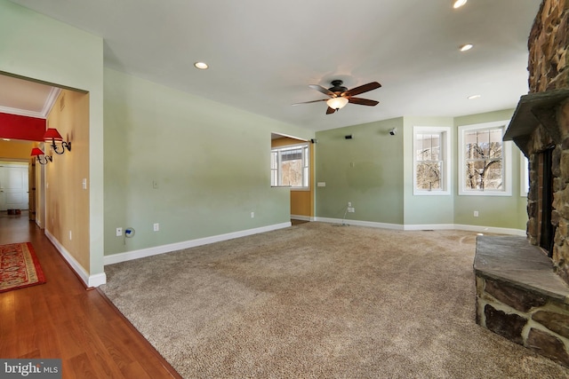 living room with a stone fireplace, ceiling fan, wood-type flooring, and ornamental molding