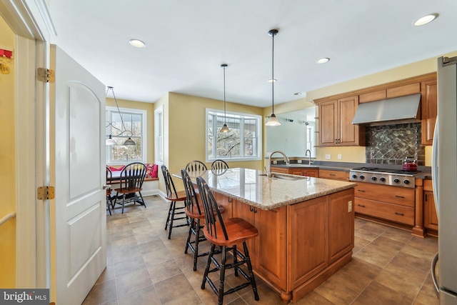 kitchen with sink, light stone countertops, an island with sink, a wealth of natural light, and range hood