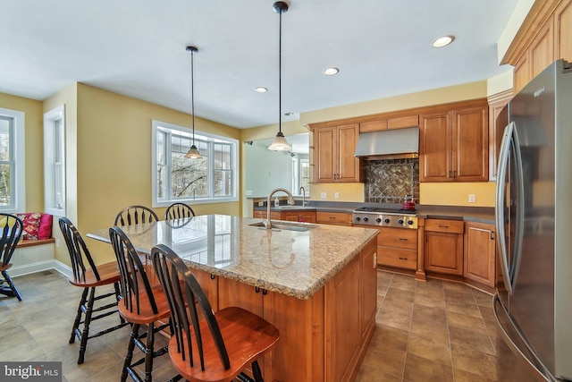 kitchen with stainless steel appliances, sink, exhaust hood, hanging light fixtures, and an island with sink