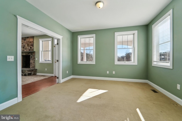 carpeted spare room with a fireplace and a healthy amount of sunlight