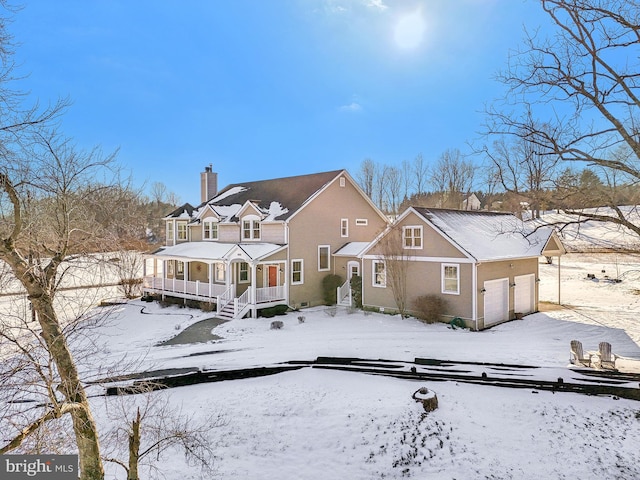 snow covered rear of property with covered porch and a garage