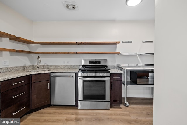 kitchen with light hardwood / wood-style floors, light stone counters, sink, and appliances with stainless steel finishes