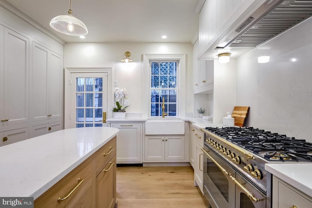 kitchen with wall chimney exhaust hood, double oven range, hanging light fixtures, white cabinetry, and sink