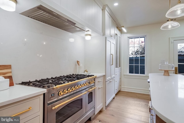 kitchen featuring hanging light fixtures, light wood-type flooring, double oven range, wall chimney exhaust hood, and white cabinetry