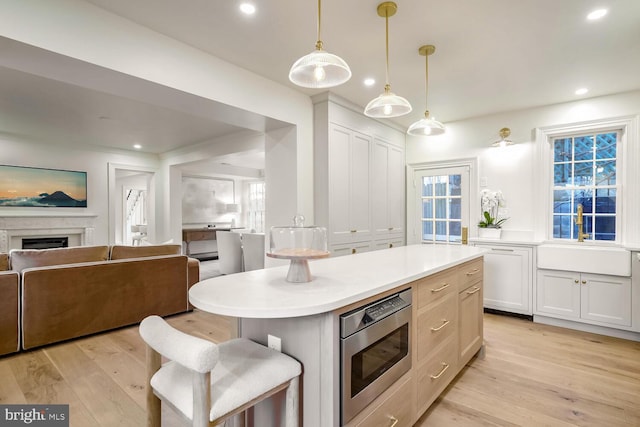 kitchen with sink, white cabinets, stainless steel microwave, and hanging light fixtures