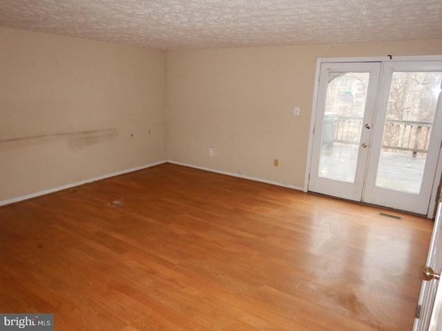 unfurnished room featuring french doors, a textured ceiling, and light wood-type flooring