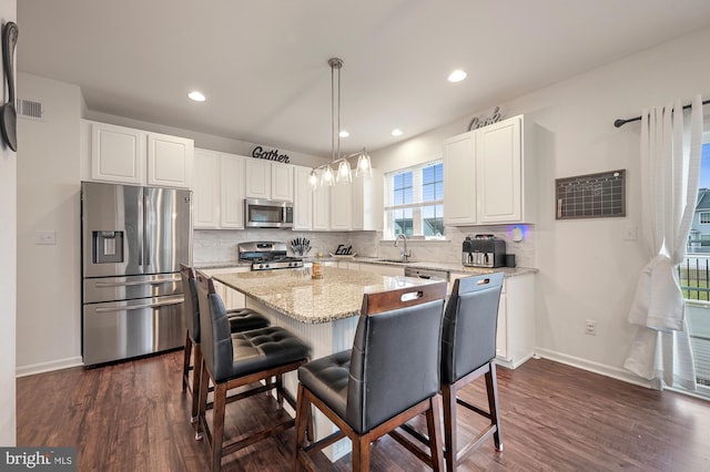 kitchen featuring appliances with stainless steel finishes, light stone counters, decorative light fixtures, white cabinets, and a center island