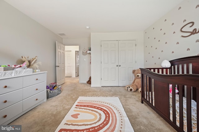 bedroom featuring a crib, light colored carpet, and a closet