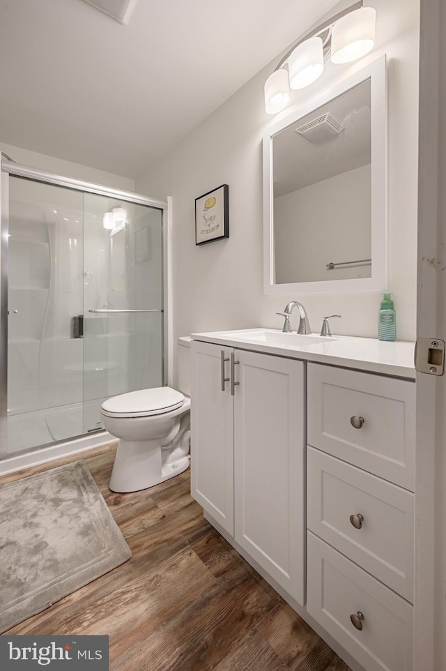 bathroom with a shower with door, vanity, wood-type flooring, and toilet