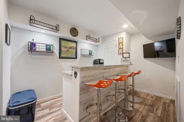 bar with light stone counters and wood-type flooring