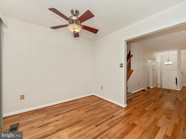 empty room featuring ceiling fan with notable chandelier and light hardwood / wood-style flooring