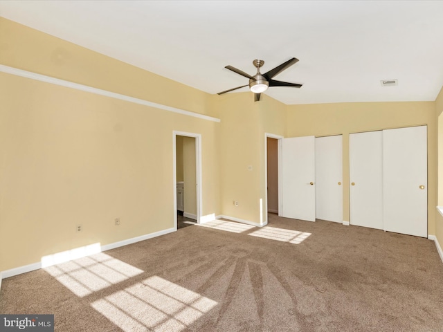 unfurnished bedroom with carpet flooring, ceiling fan, vaulted ceiling, and multiple closets