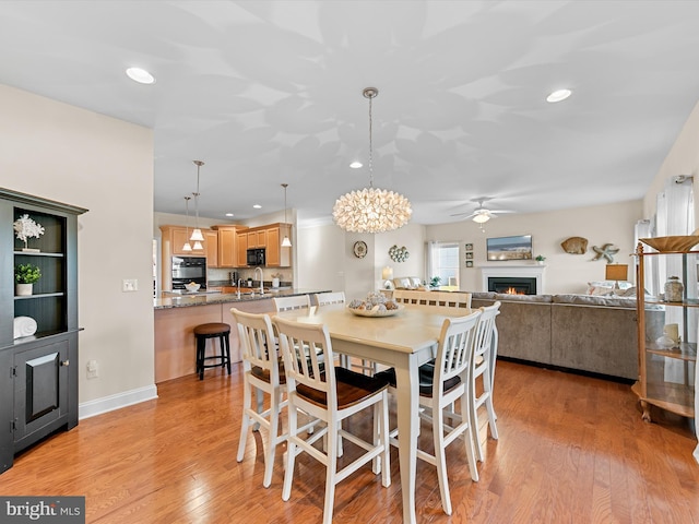 dining space with light wood-type flooring, ceiling fan with notable chandelier, and sink