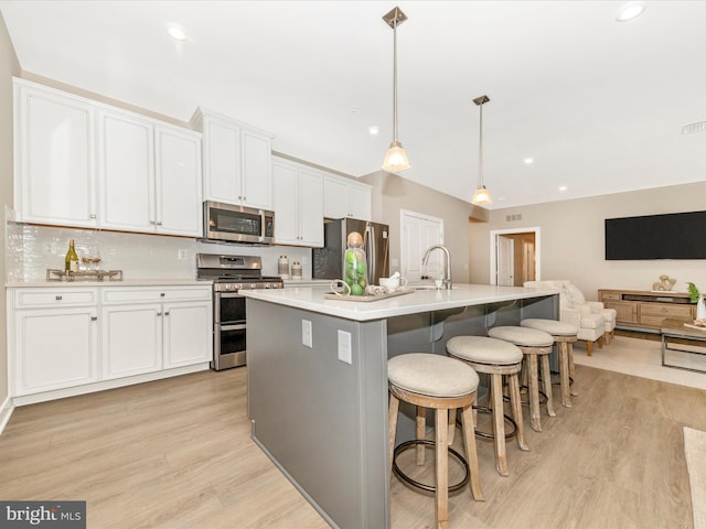 kitchen with white cabinetry, a center island with sink, stainless steel appliances, and decorative light fixtures