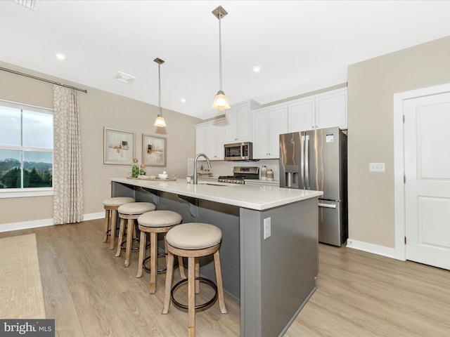 kitchen with stainless steel appliances, sink, white cabinets, hanging light fixtures, and an island with sink