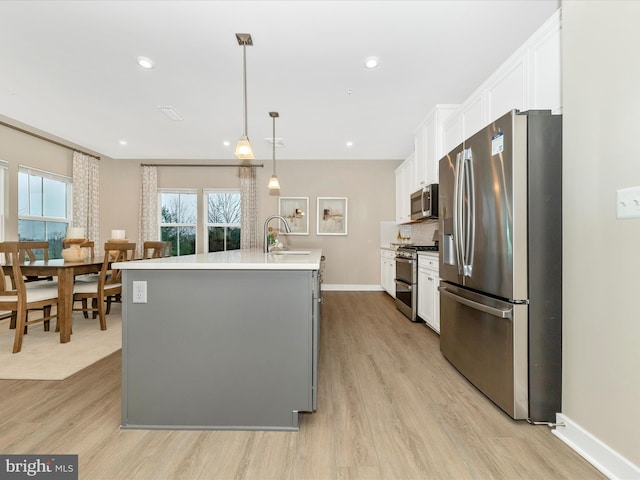 kitchen featuring white cabinetry, stainless steel appliances, light hardwood / wood-style flooring, decorative light fixtures, and a kitchen island with sink