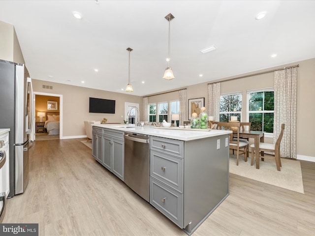 kitchen with appliances with stainless steel finishes, a kitchen island with sink, sink, decorative light fixtures, and gray cabinets